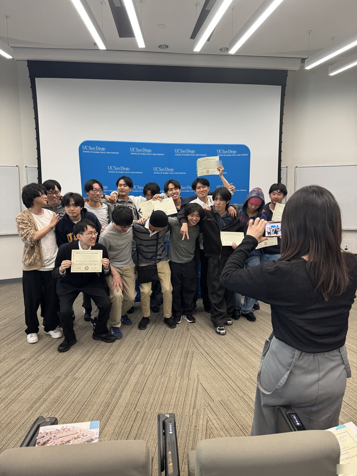 Participants posing with their certificates at the closing ceremony, in front of a UC San Diego backdrop