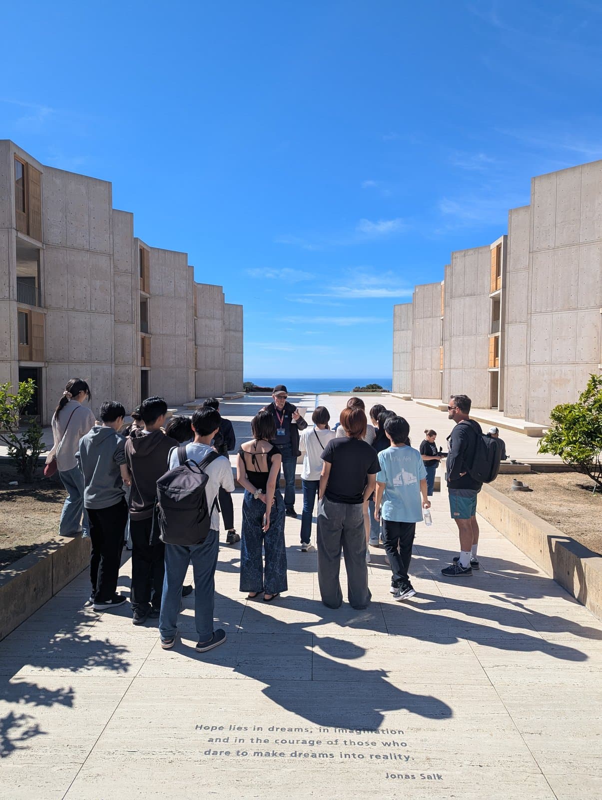 Participants listening to a guide in the Salk Institute courtyard, with the Pacific beyond