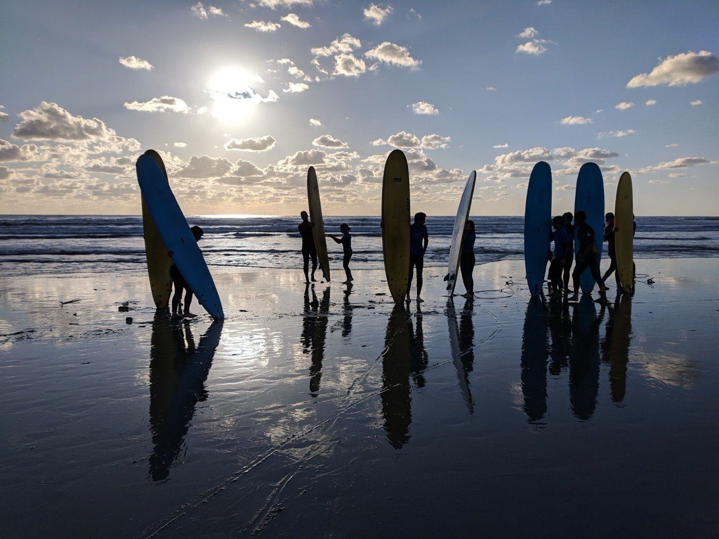 Silhouettes of FGL students holding surfboards on the beach at sunset